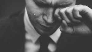 Image of a distraught man wiping his left eye with his left hand.
